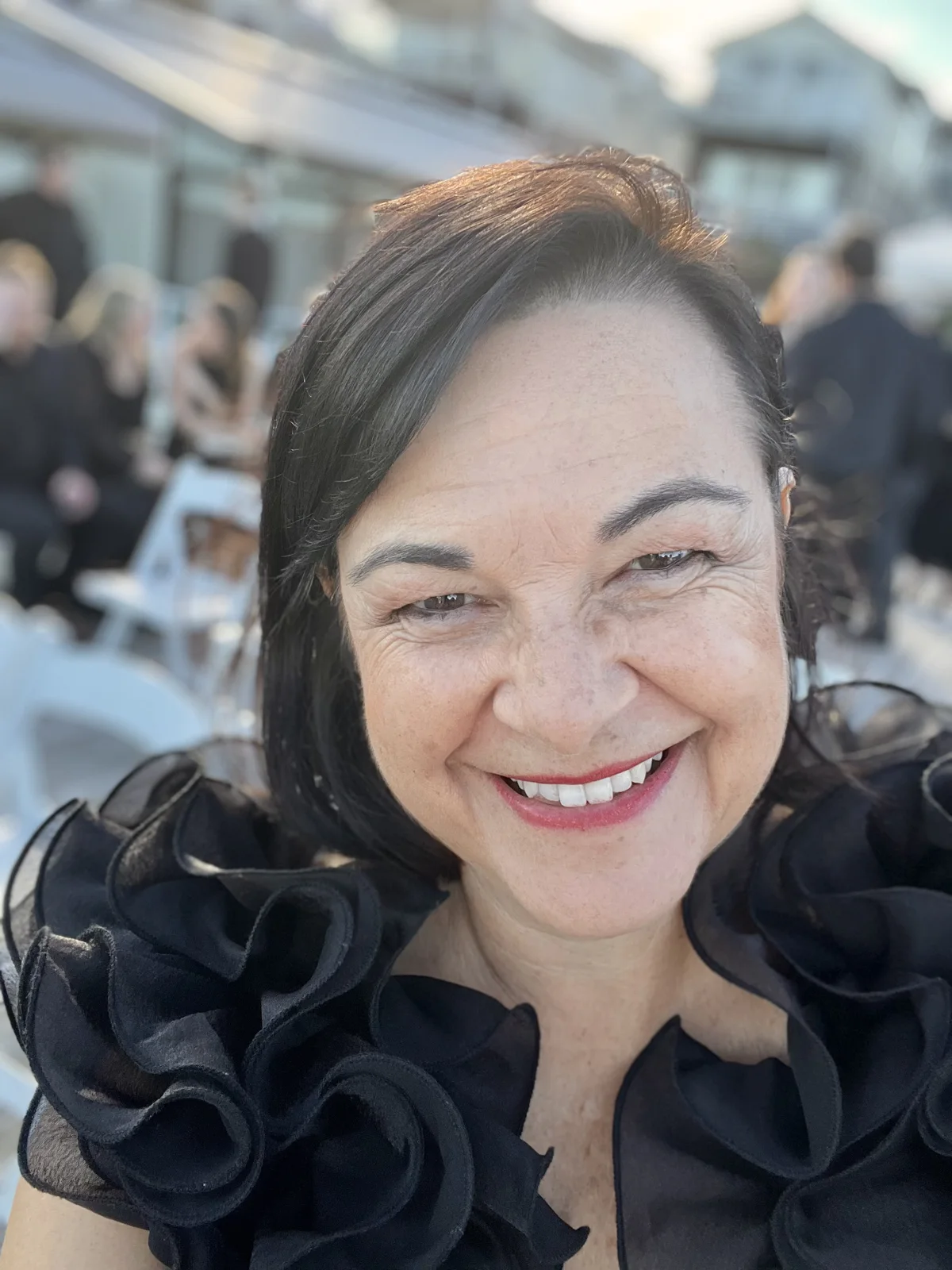 Angela smiling in a black ruffled top at a wedding.