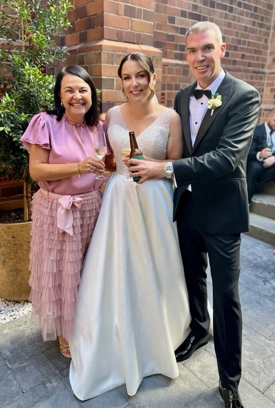 Angela in pink with a couple beside a brick building.