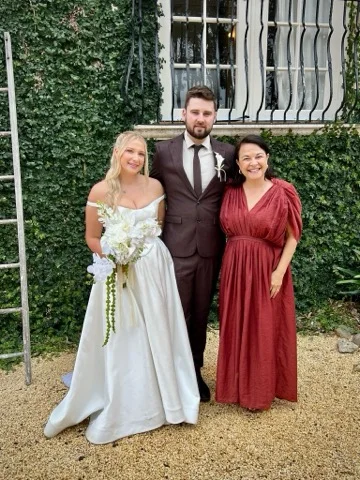 Angela with a wedding couple outside an ivy-covered building.