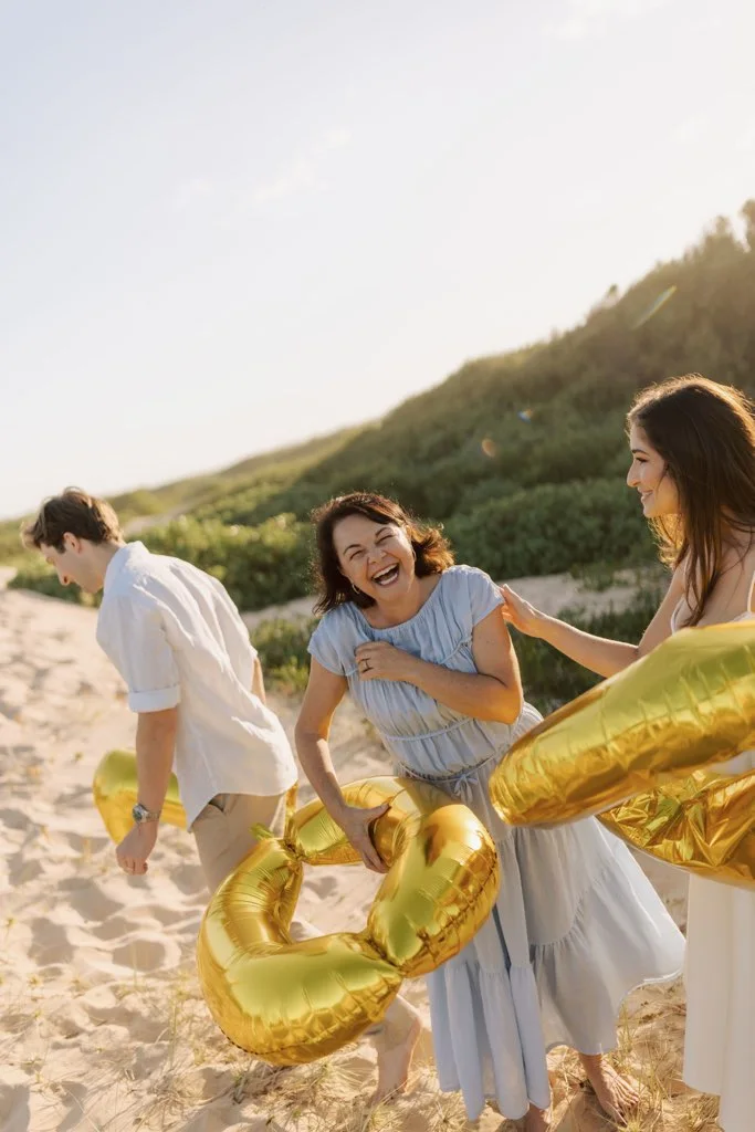 Angela celebrating on the beach with a couple and gold balloons.