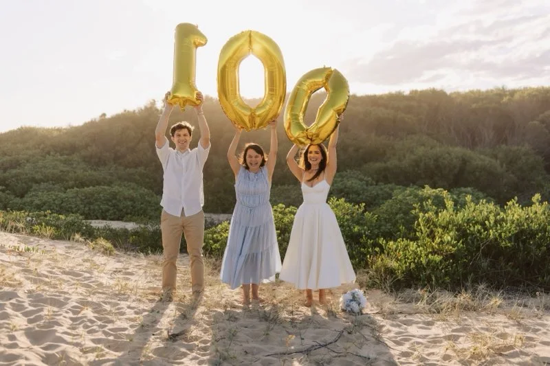 Angela with a couple holding gold balloons on the beach.