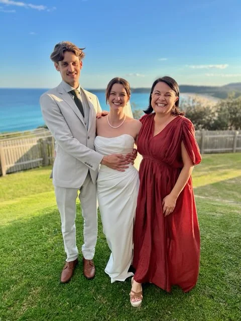 Angela with a wedding couple on a coastal lawn.