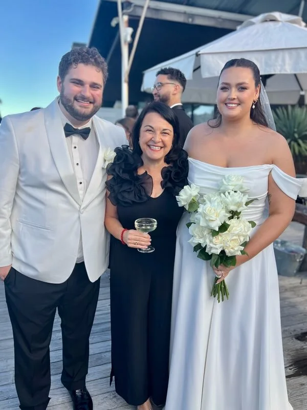 Angela in black with a couple holding wedding flowers.