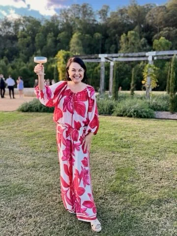 Angela raising a glass on a garden lawn.