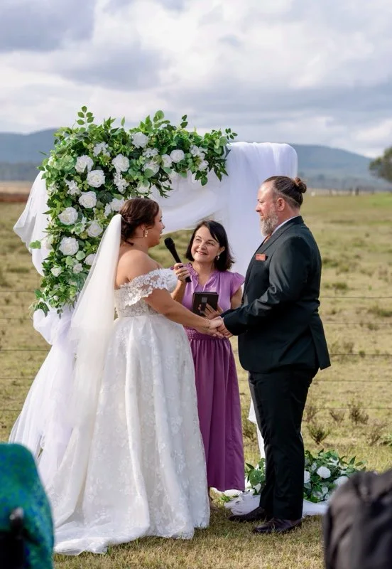 Angela officiating a countryside wedding beneath a floral arch.