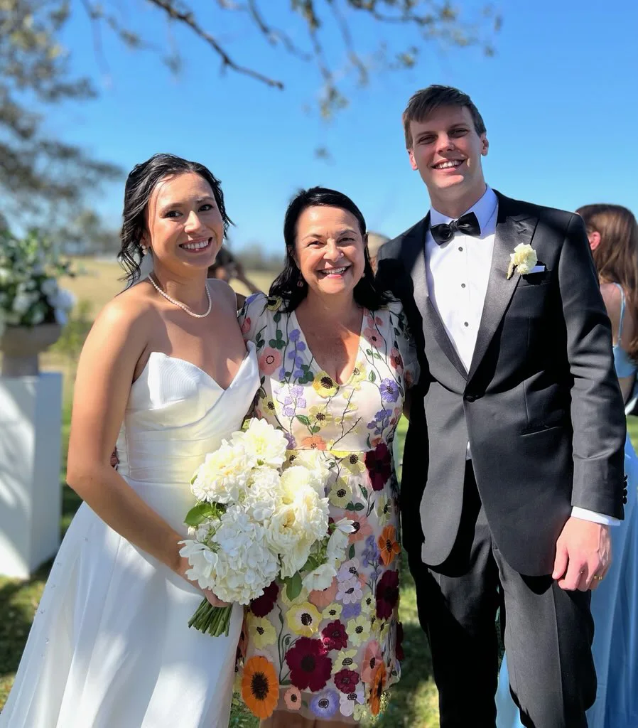 Angela with a bride and her groom in a black tuxedo.