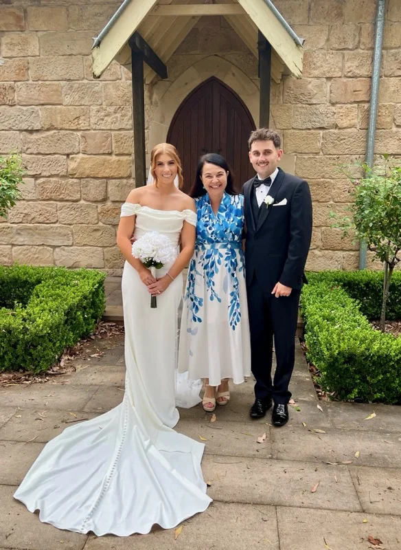 Angela with a wedding couple outside a sandstone chapel.