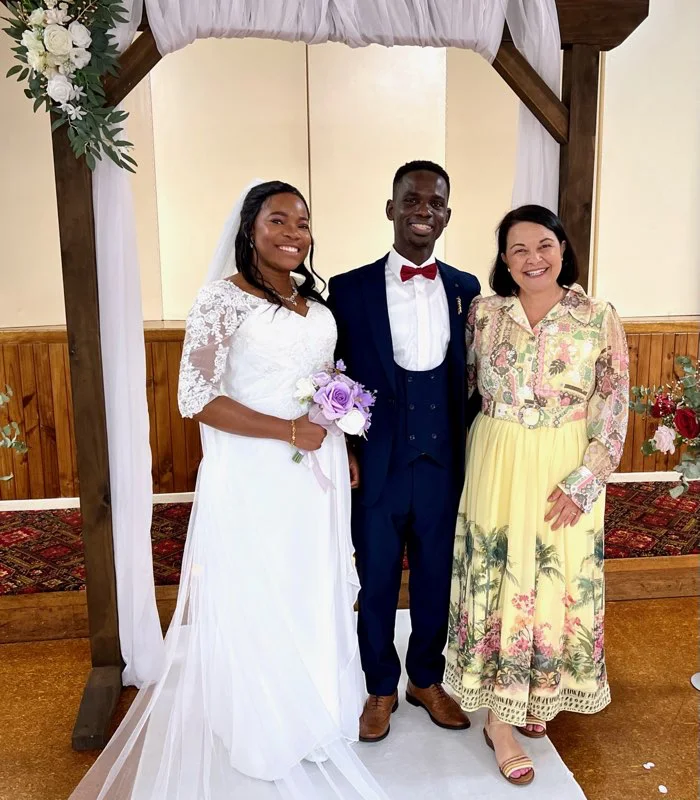 Angela with a wedding couple under a draped timber arbour.