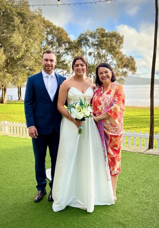 Angela with a wedding couple on a waterside lawn.