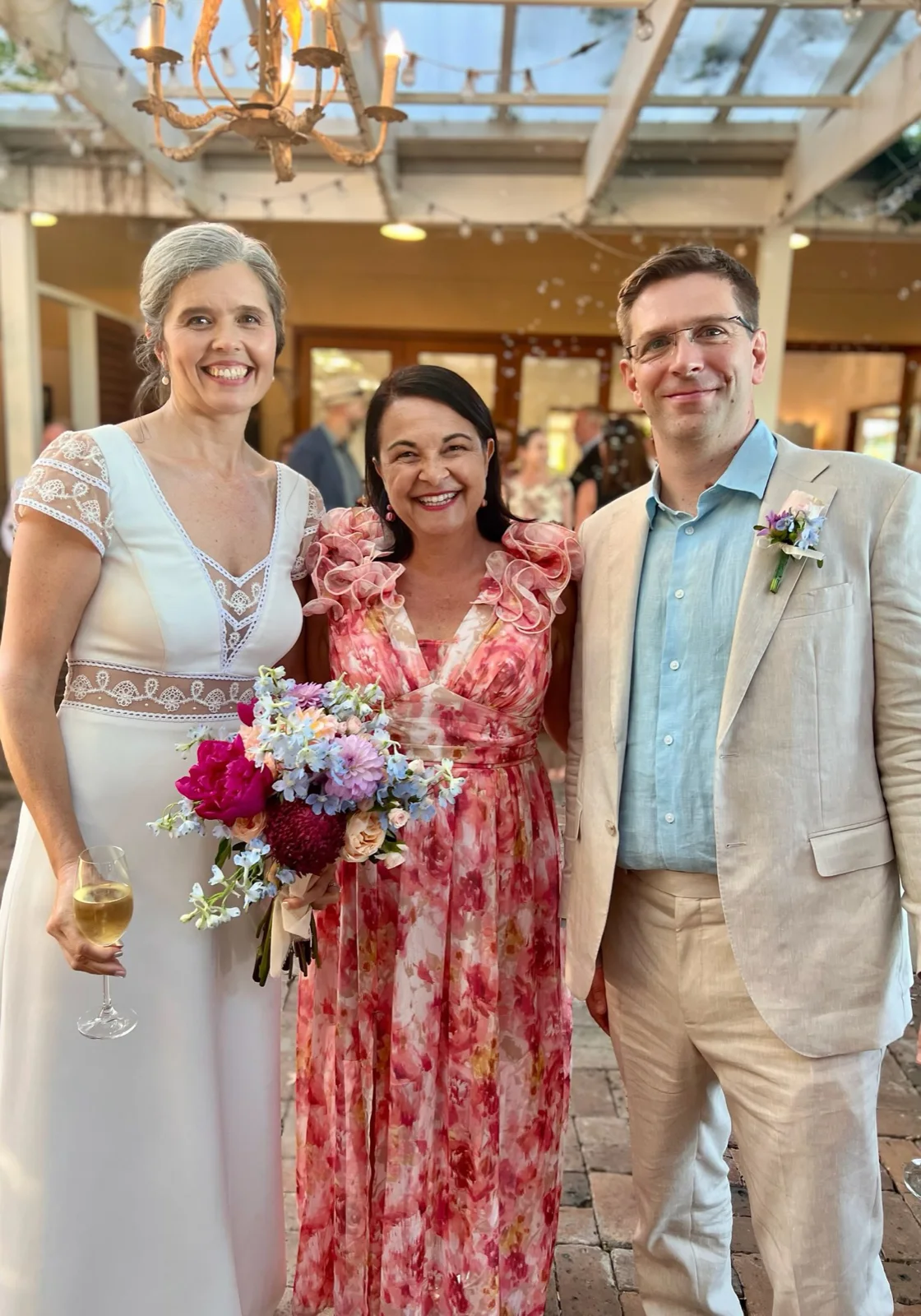 Angela in a floral dress with a wedding couple under a glass roof.