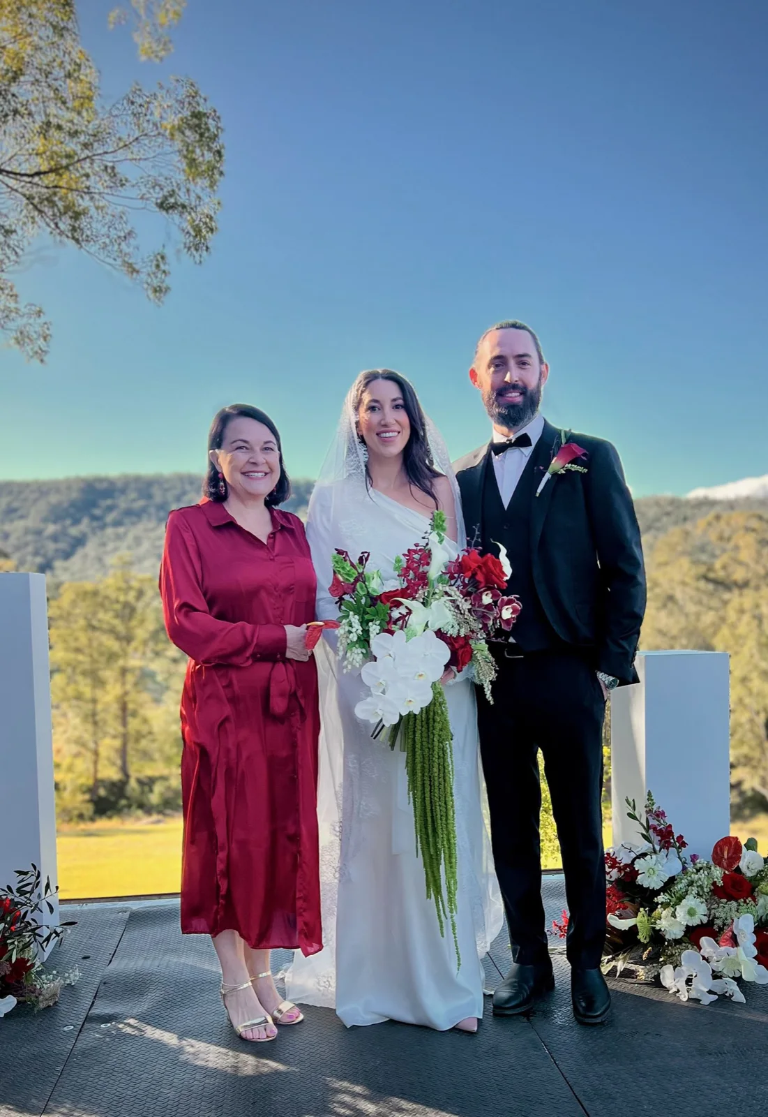 Angela in red with a wedding couple above a valley view.