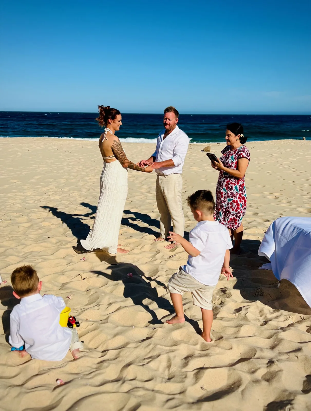 A small beach ceremony with Angela, the couple and children on the sand.