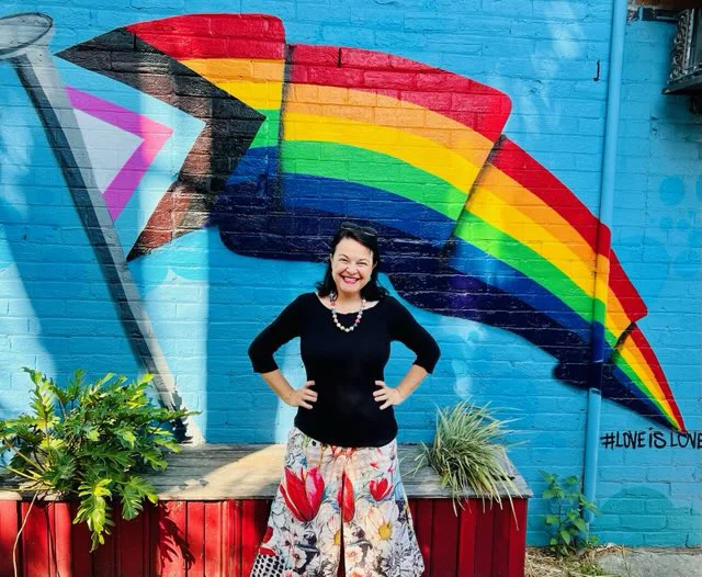 Angela smiling in front of a rainbow mural.