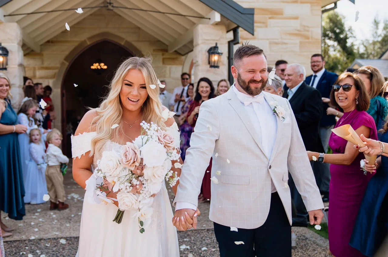 The newlyweds walking out through cheering guests and petals.