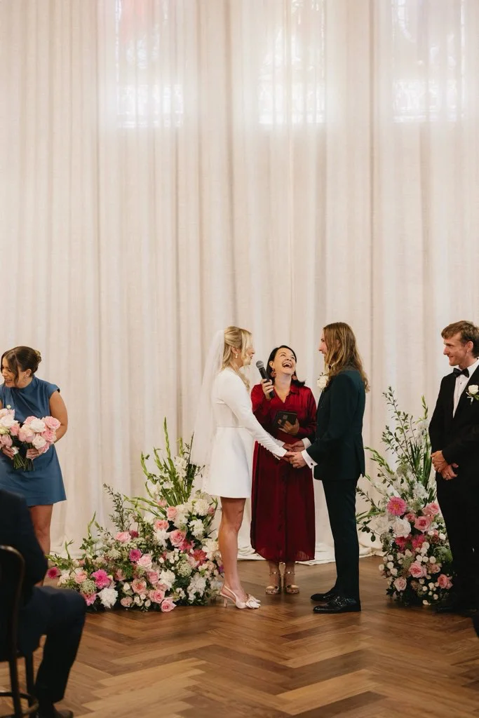 Angela leading an indoor ceremony framed by pink flowers.