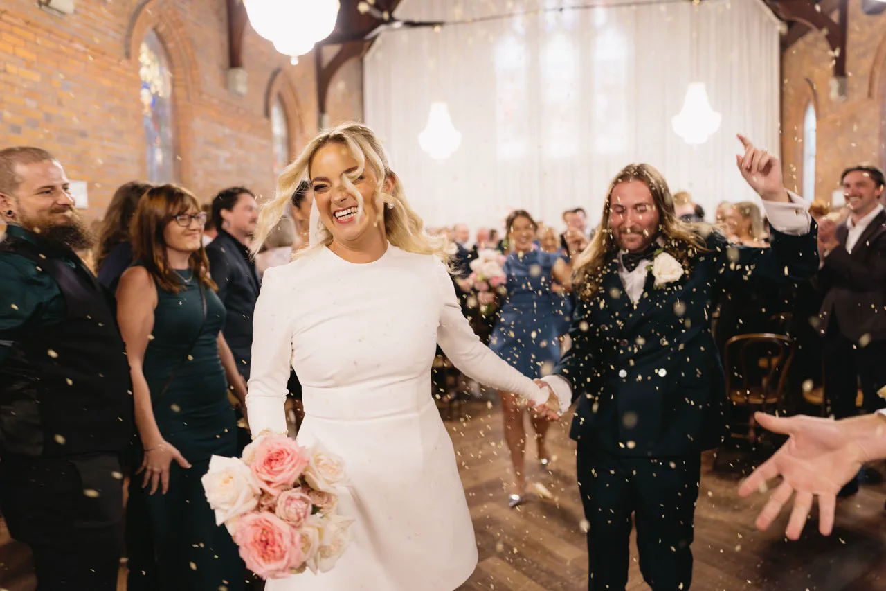 The newlyweds dancing up the aisle through confetti.