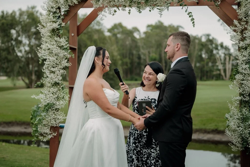 Angela with a couple exchanging vows under a flowered arbour.