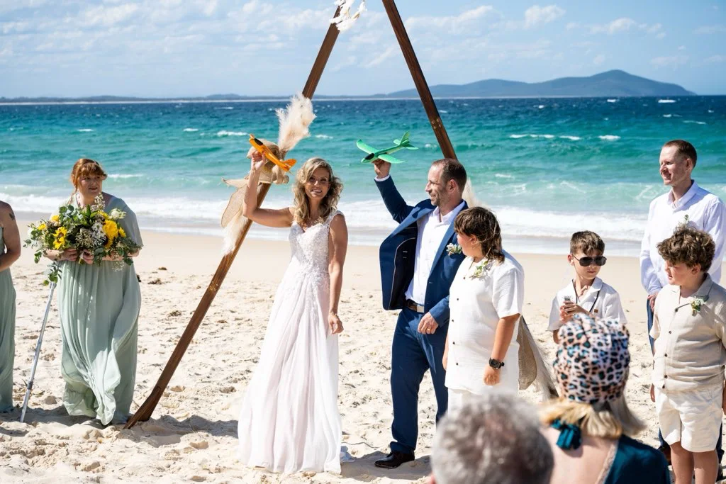 The couple celebrating at a beach ceremony by a timber arbour.