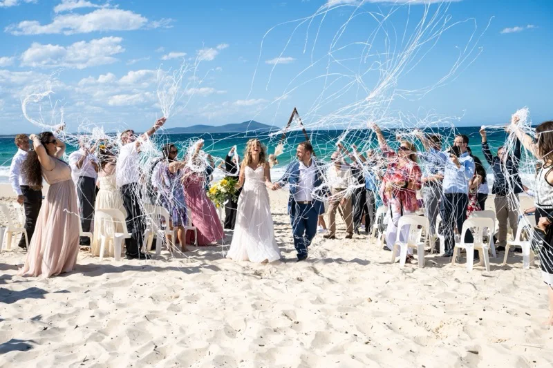 Guests cheering the couple down a beach aisle with streamers.