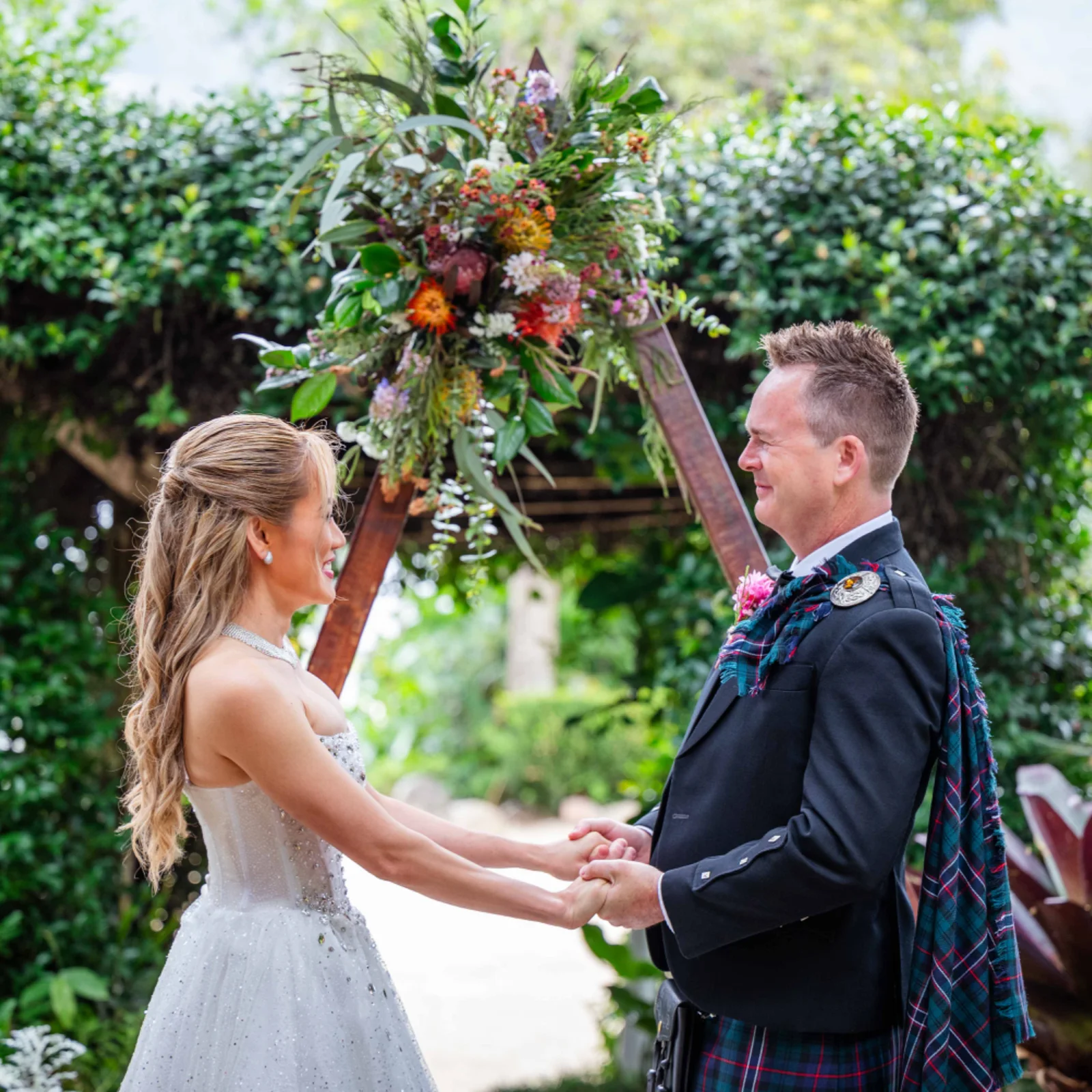A couple exchanging vows beneath a colourful garden ceremony arch.