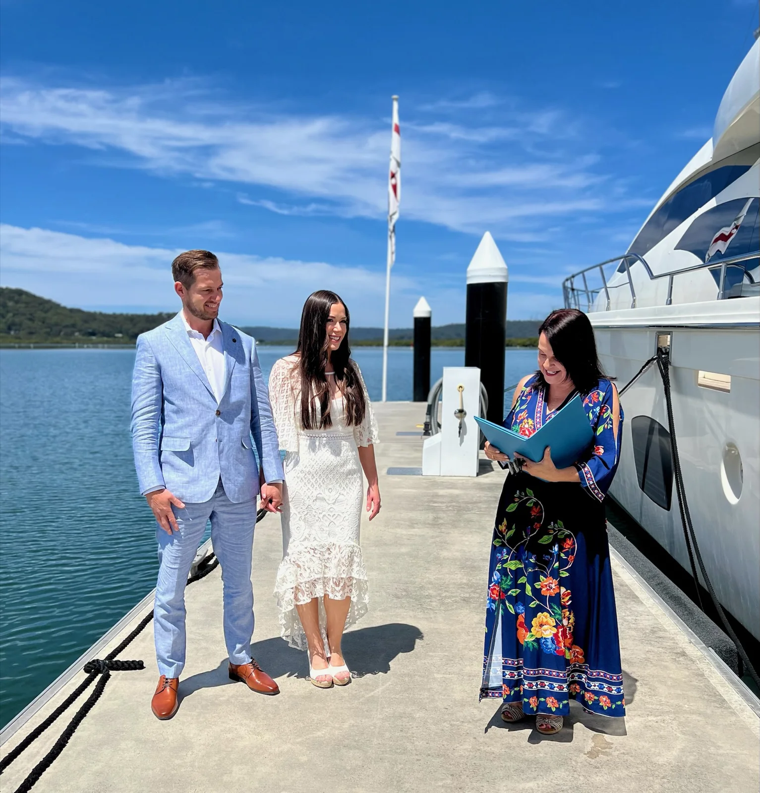 Angela with a wedding couple on a sunny marina jetty.